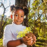 criança segurando muda de árvore ao morar perto de áreas verdes