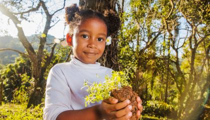criança segurando muda de árvore ao morar perto de áreas verdes